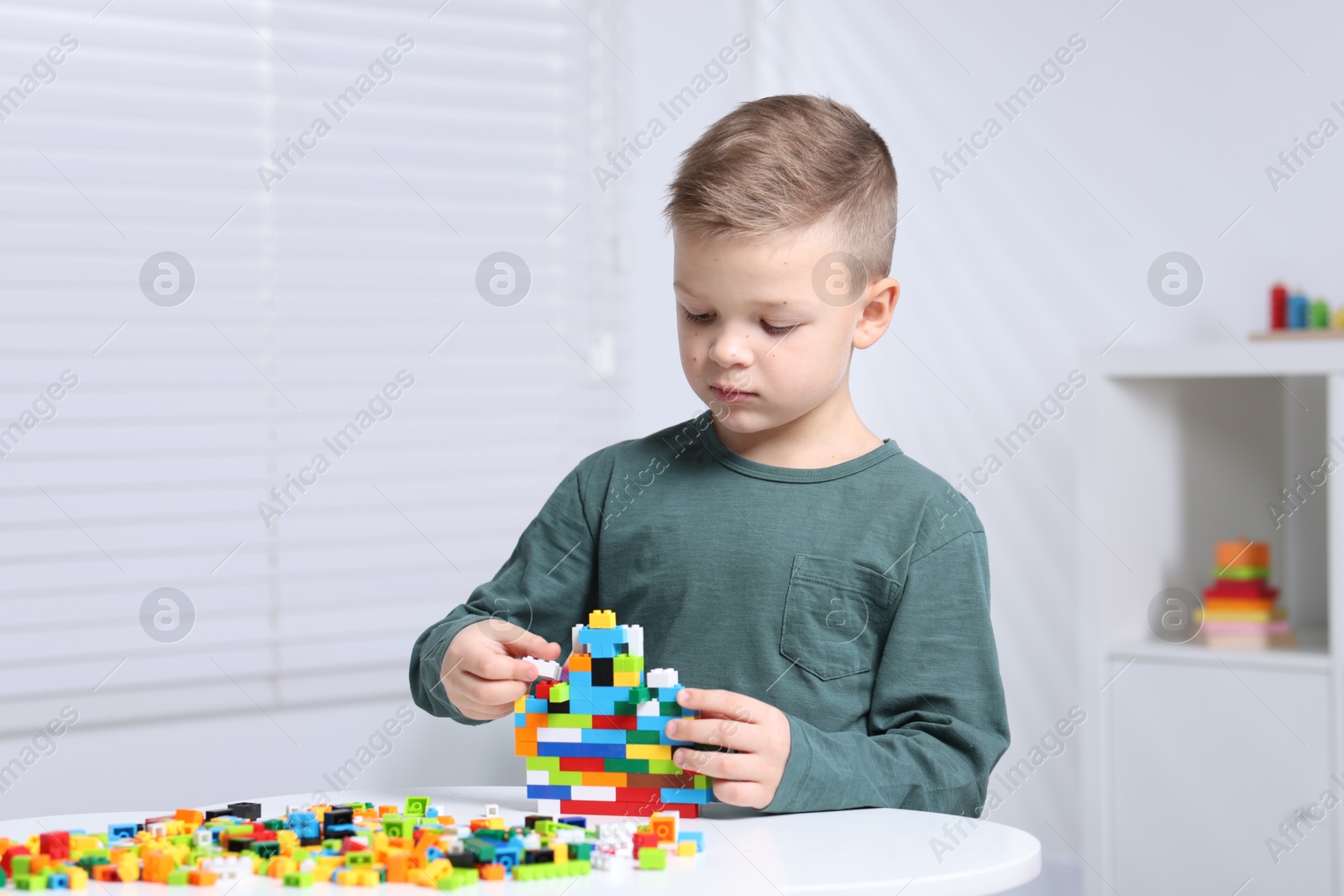 Photo of Cute boy playing with building blocks at white table indoors. Space for text