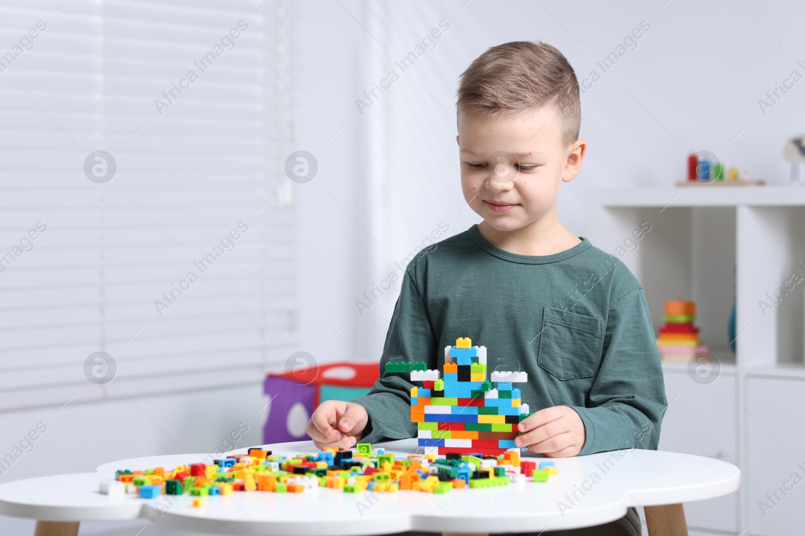 Photo of Cute boy playing with building blocks at white table indoors. Space for text