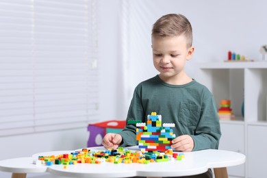 Photo of Cute boy playing with building blocks at white table indoors. Space for text