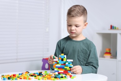 Cute boy playing with building blocks at white table indoors. Space for text