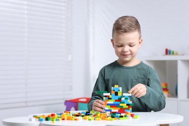 Photo of Cute boy playing with building blocks at white table indoors. Space for text