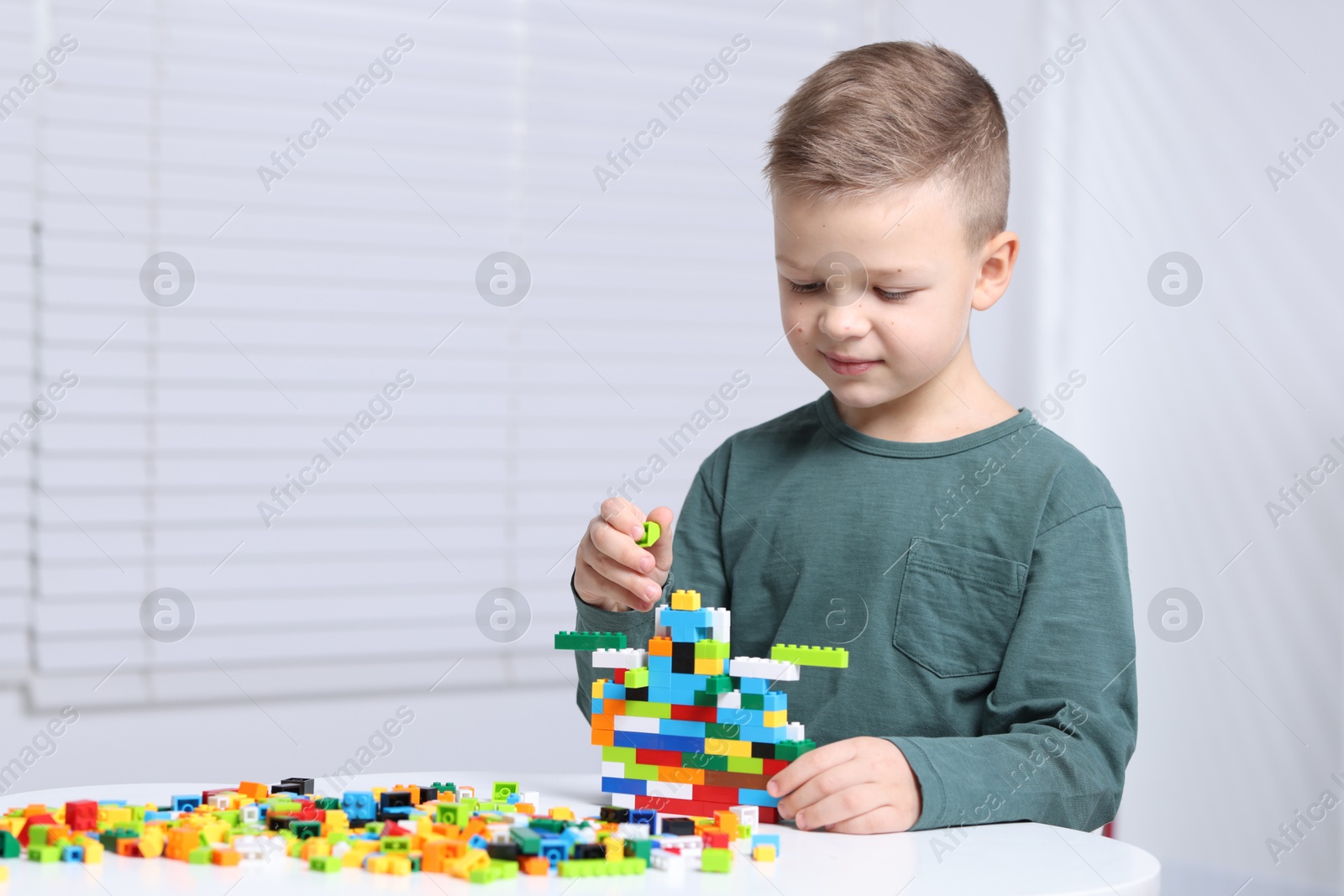 Photo of Cute boy playing with building blocks at white table indoors. Space for text