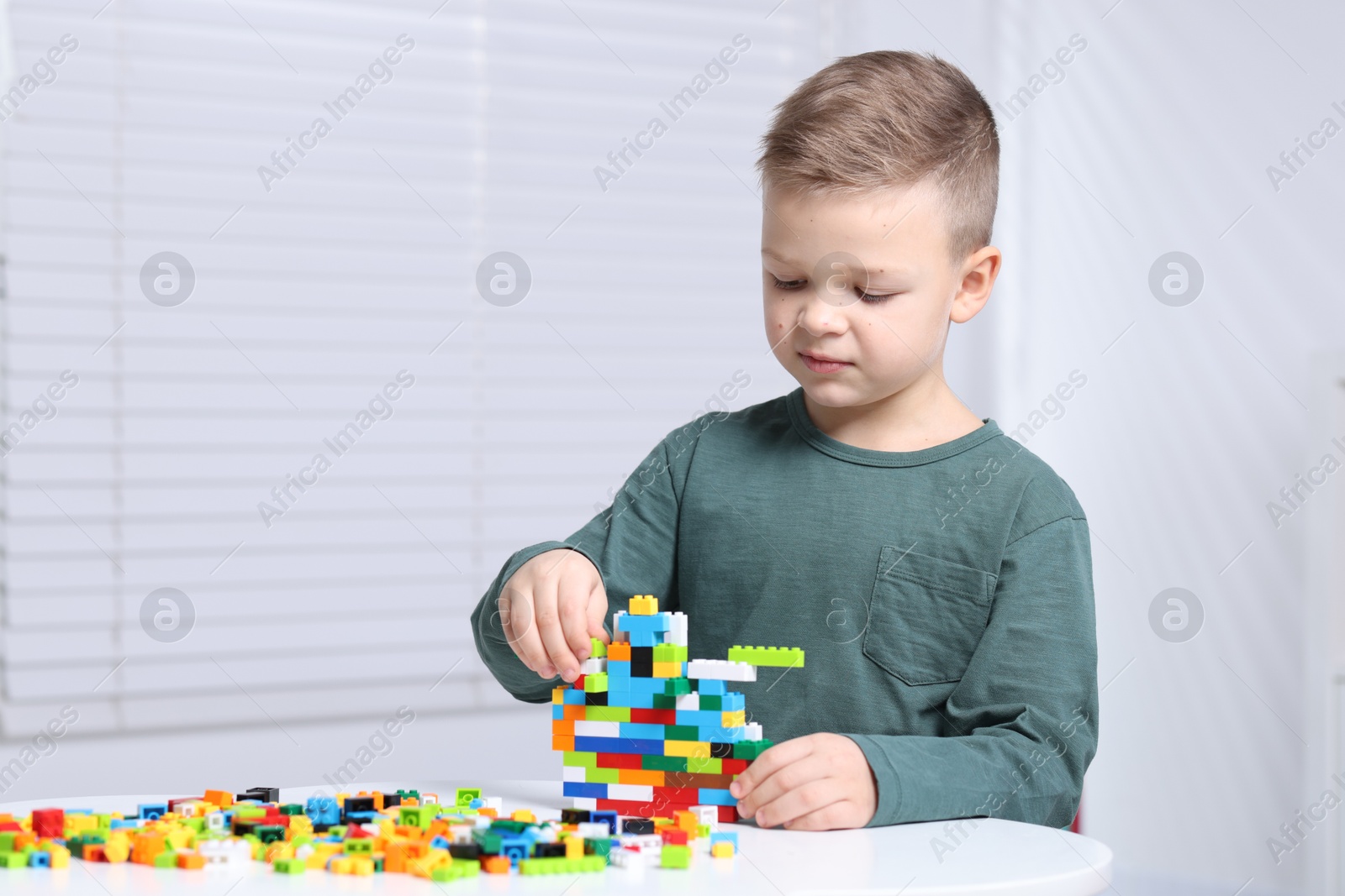 Photo of Cute boy playing with building blocks at white table indoors. Space for text