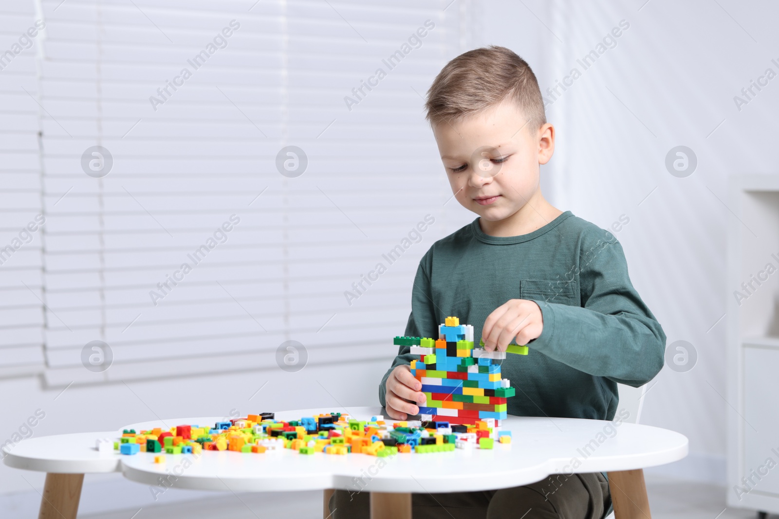 Photo of Cute boy playing with building blocks at white table indoors. Space for text