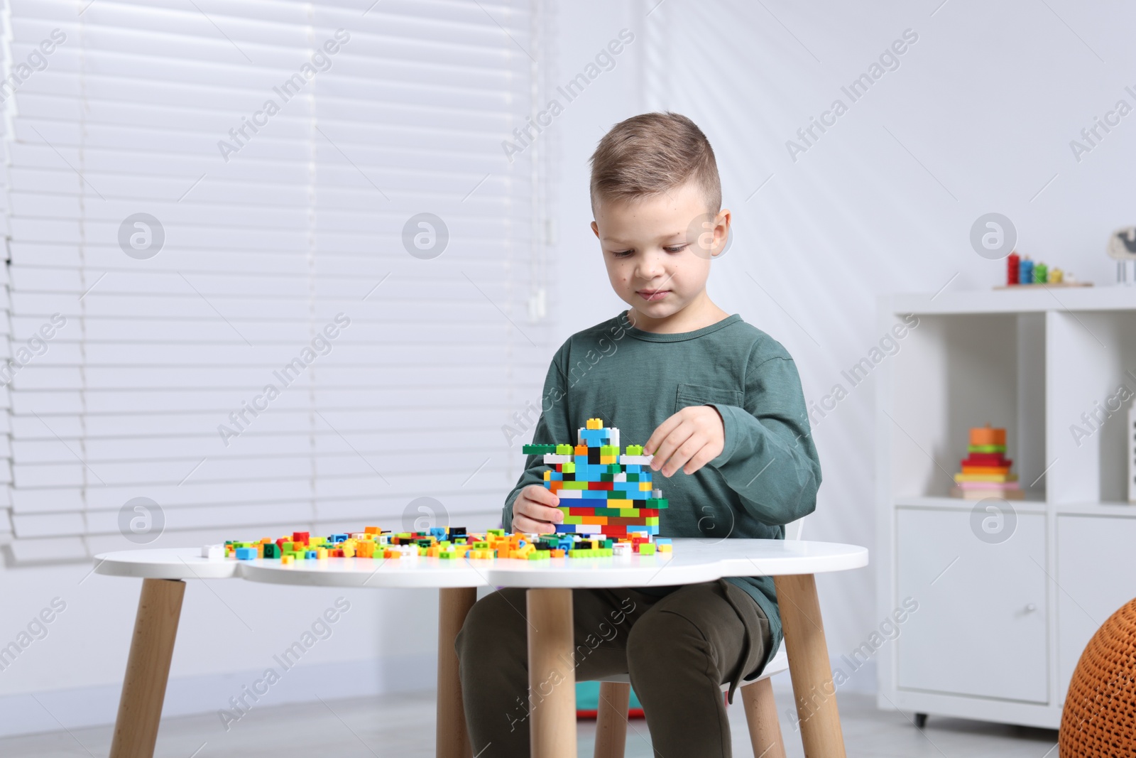 Photo of Cute boy playing with building blocks at white table indoors. Space for text