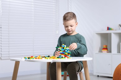 Photo of Cute boy playing with building blocks at white table indoors. Space for text