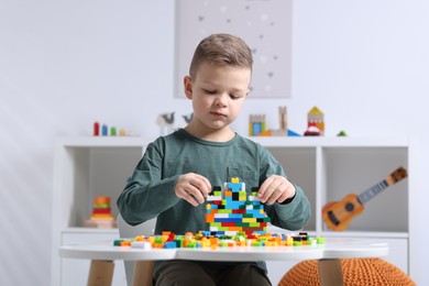 Photo of Cute boy playing with building blocks at white table indoors