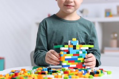 Photo of Cute boy playing with building blocks at white table indoors, closeup