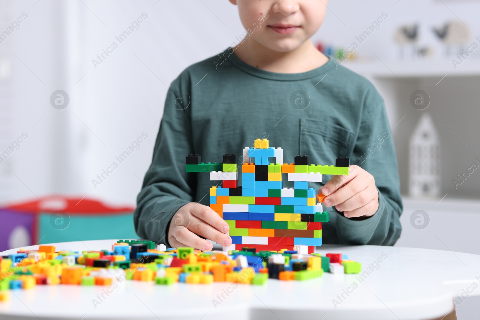 Photo of Cute boy playing with building blocks at white table indoors, closeup