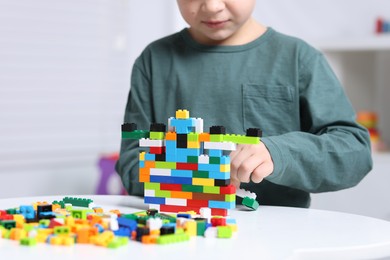 Photo of Cute boy playing with building blocks at white table indoors, closeup