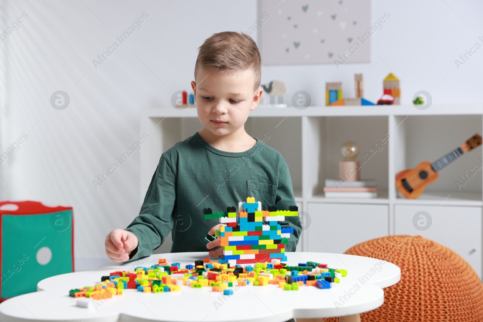 Photo of Cute boy playing with building blocks at white table indoors