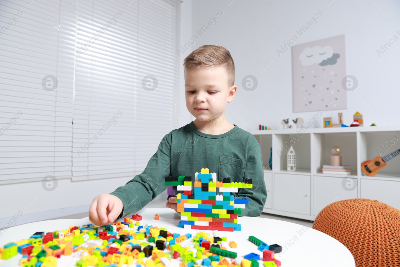 Photo of Cute boy playing with building blocks at white table indoors