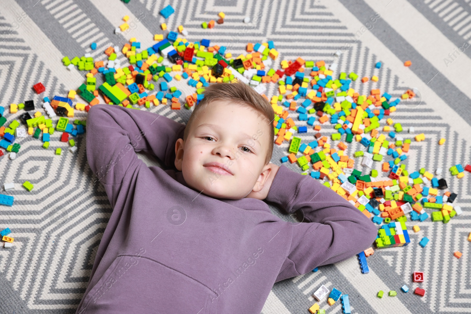 Photo of Cute boy and colorful building blocks on floor, top view