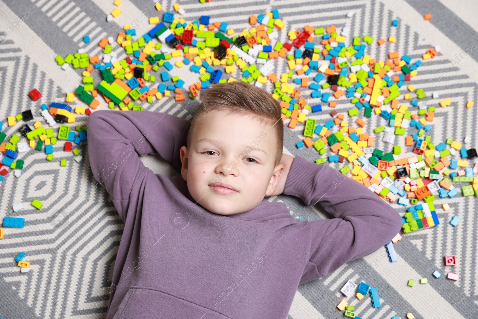 Photo of Cute boy and colorful building blocks on floor, top view