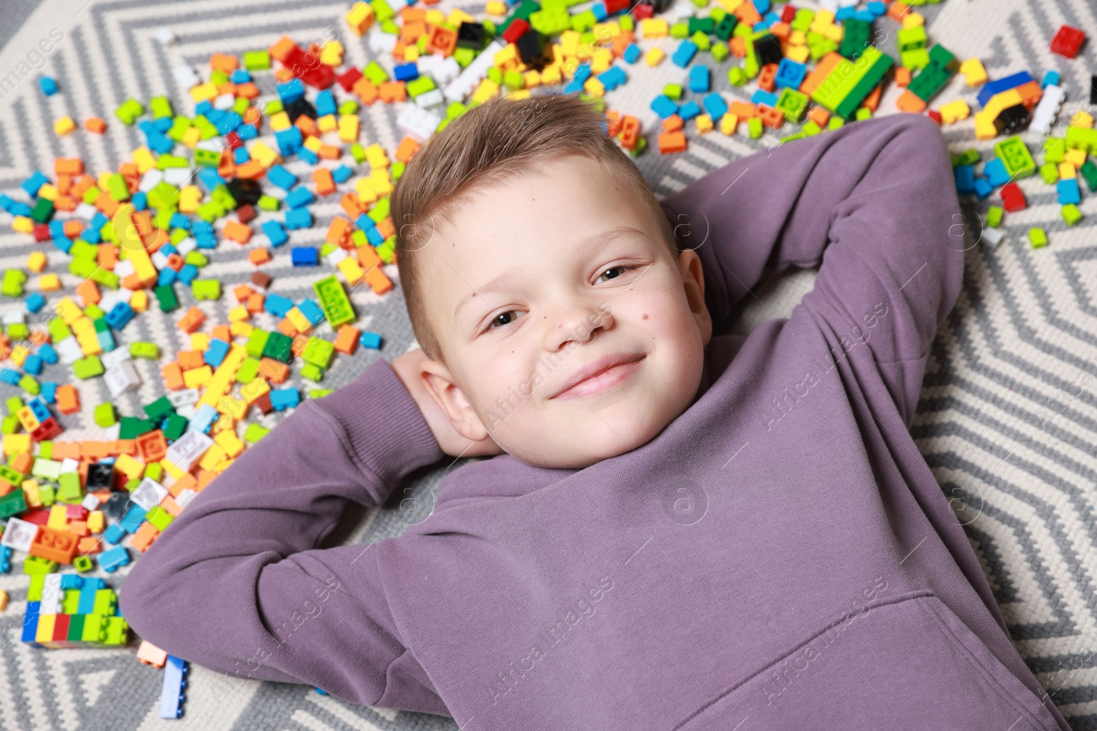 Photo of Cute boy and colorful building blocks on floor, top view