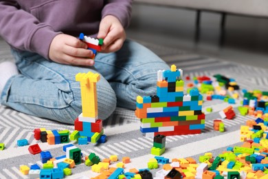 Photo of Cute boy playing with building blocks on floor at home, closeup