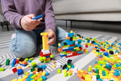 Photo of Cute boy playing with building blocks on floor at home, closeup