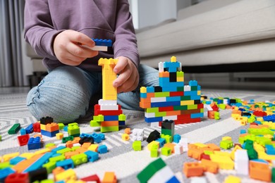 Photo of Cute boy playing with building blocks on floor at home, closeup