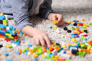 Photo of Cute boy playing with building blocks on floor at home, closeup