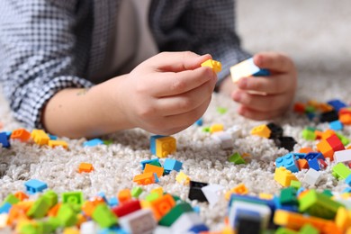 Photo of Cute boy playing with building blocks on floor at home, closeup