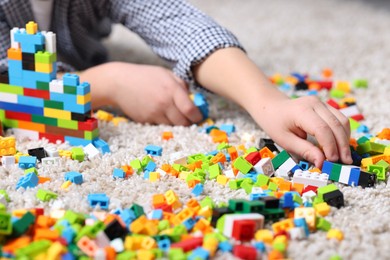 Photo of Cute boy playing with building blocks on floor at home, closeup