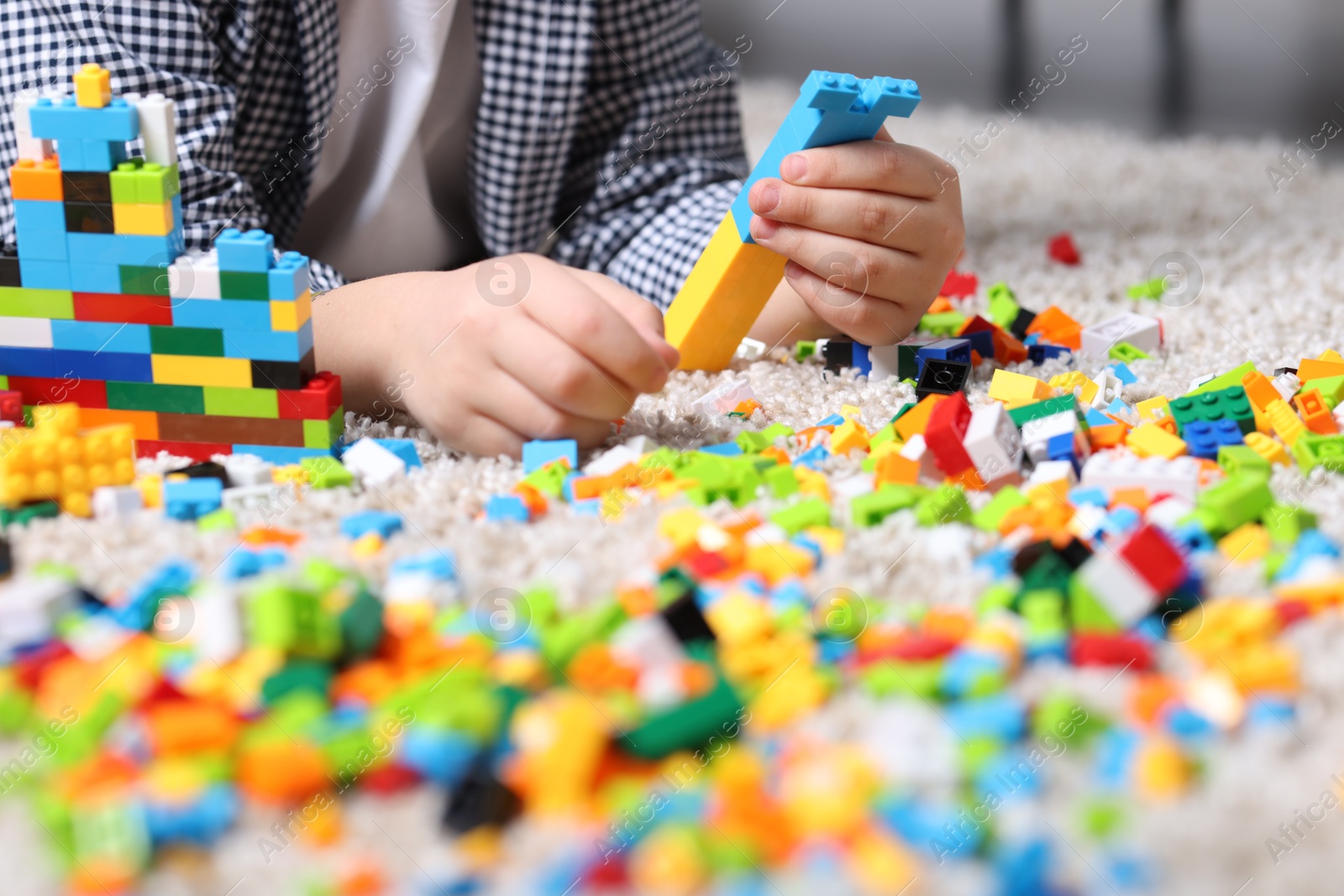 Photo of Cute boy playing with building blocks on floor at home, closeup