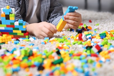 Photo of Cute boy playing with building blocks on floor at home, closeup