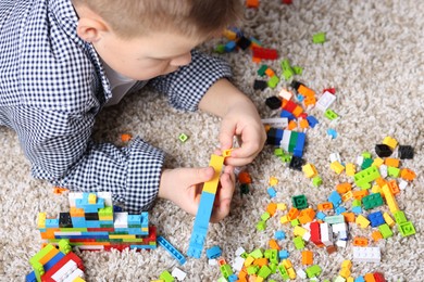 Photo of Cute boy playing with building blocks on floor at home, closeup