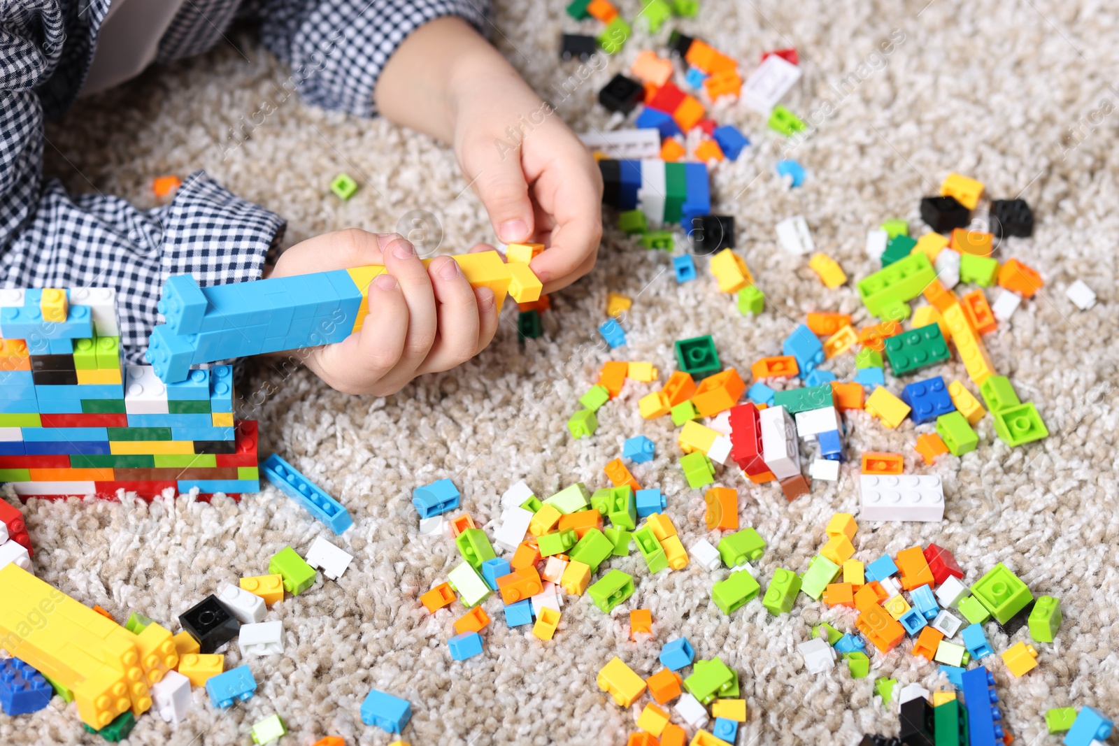 Photo of Cute boy playing with building blocks on floor at home, closeup