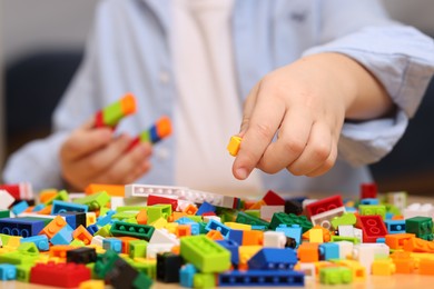 Photo of Cute boy playing with building blocks at wooden table indoors, closeup