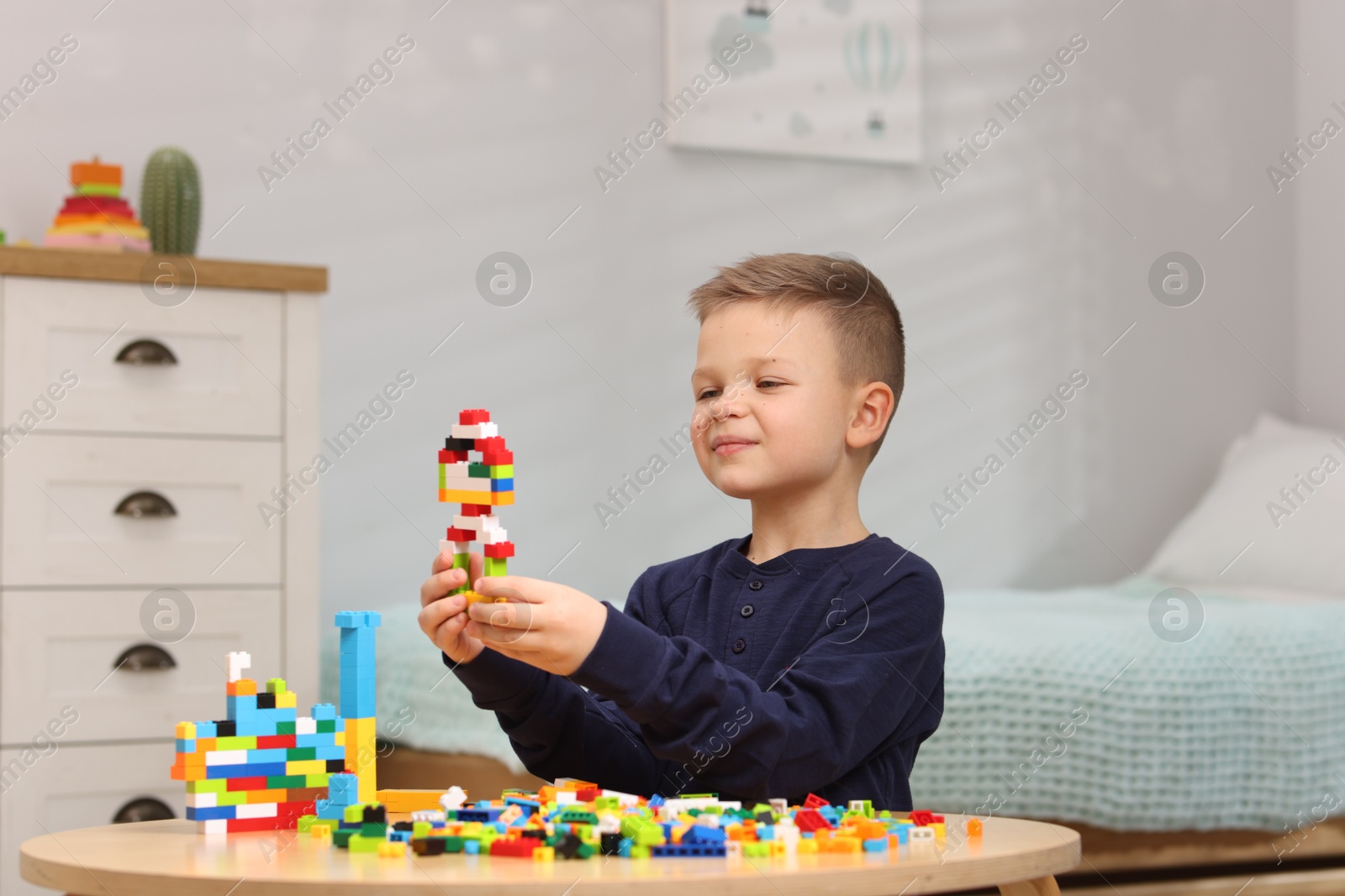 Photo of Cute boy playing with building blocks at wooden table indoors