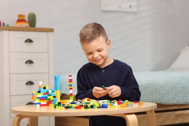 Photo of Cute boy playing with building blocks at wooden table indoors