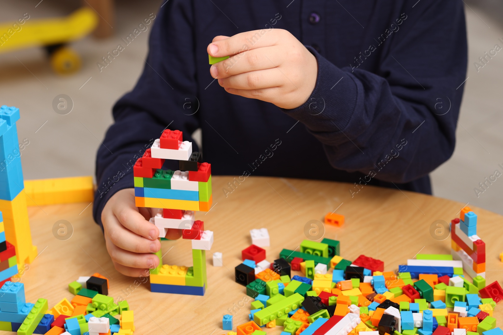 Photo of Cute boy playing with building blocks at wooden table indoors, closeup