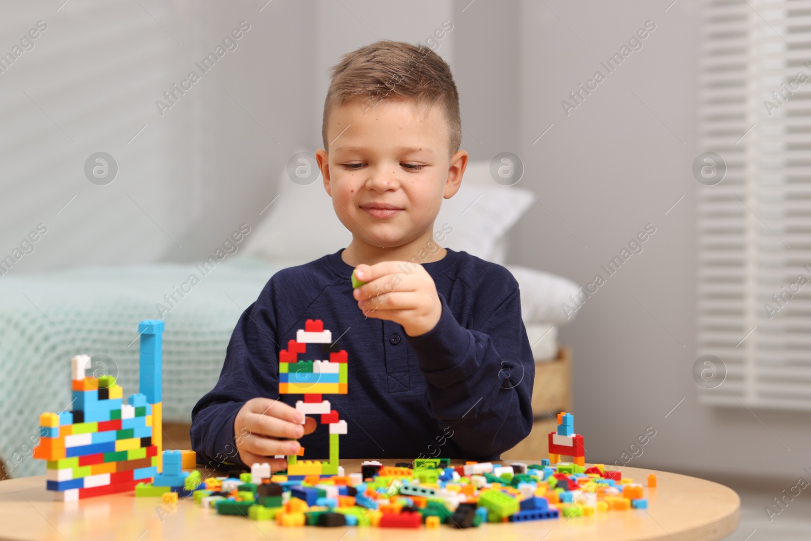 Photo of Cute boy playing with building blocks at wooden table indoors