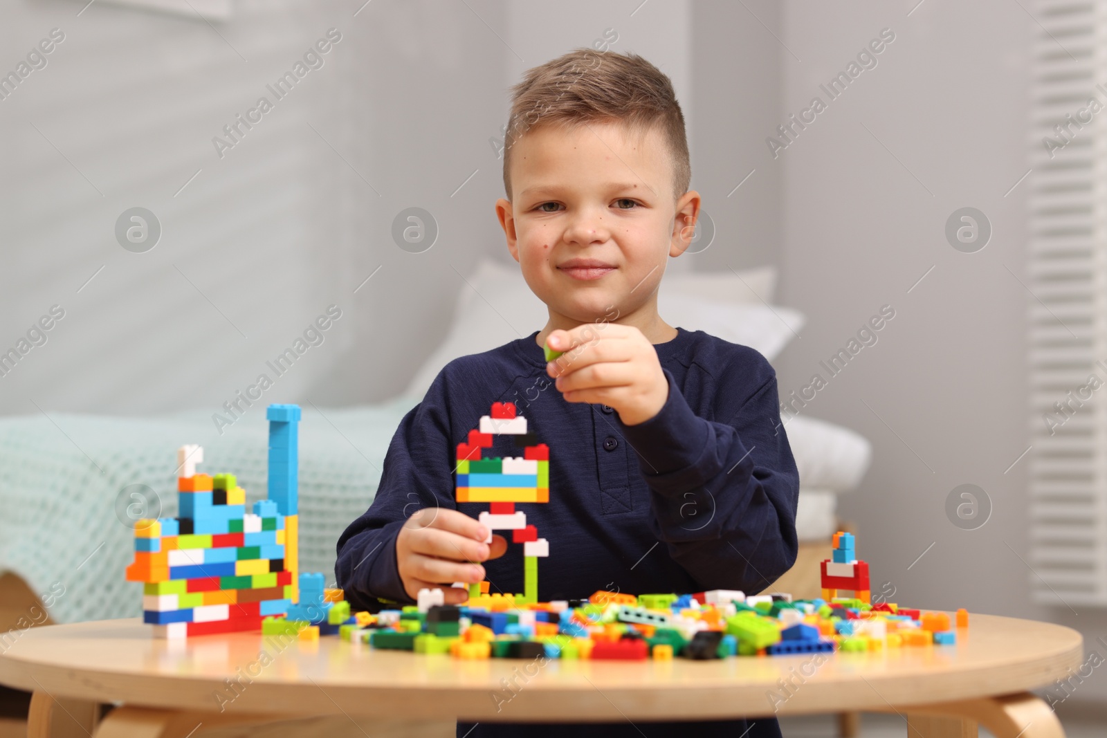 Photo of Cute boy playing with building blocks at wooden table indoors