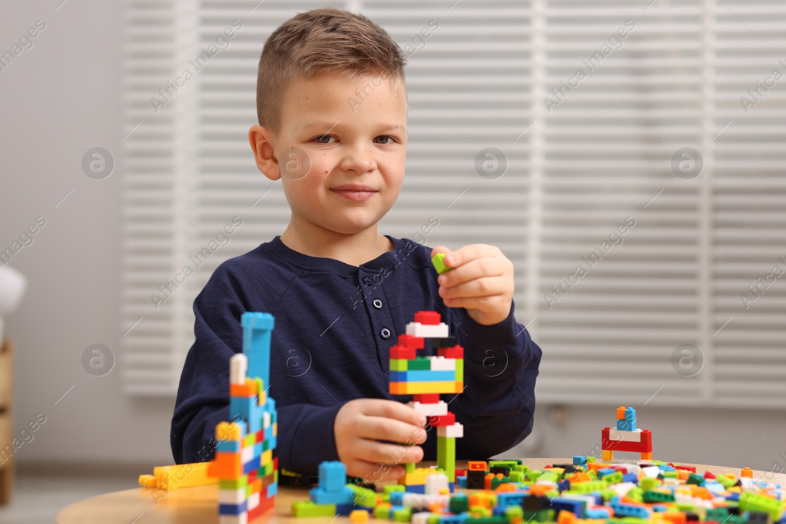 Photo of Cute boy playing with building blocks at wooden table indoors