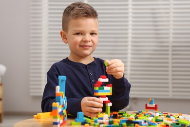 Photo of Cute boy playing with building blocks at wooden table indoors