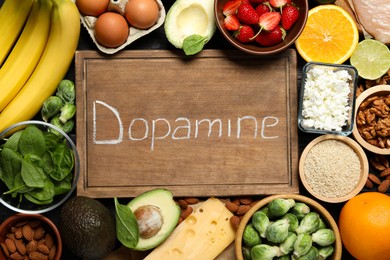 Wooden board with word Dopamine and different products as background, closeup