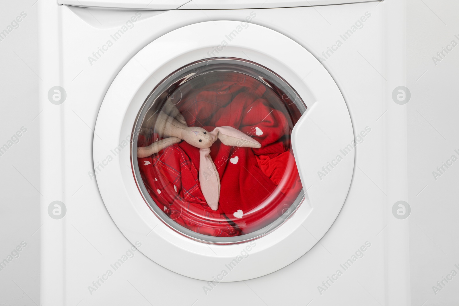 Photo of Washing machine with clothes and toy bunny as background, closeup