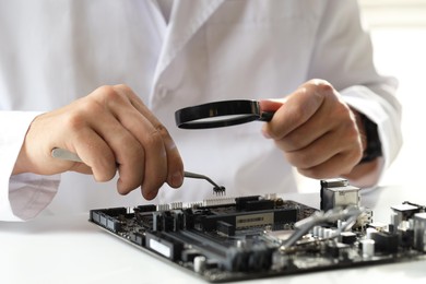 Photo of Man with magnifying glass installing computer chip onto motherboard at white table, closeup