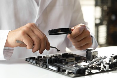 Photo of Man with magnifying glass installing computer chip onto motherboard at white table, closeup