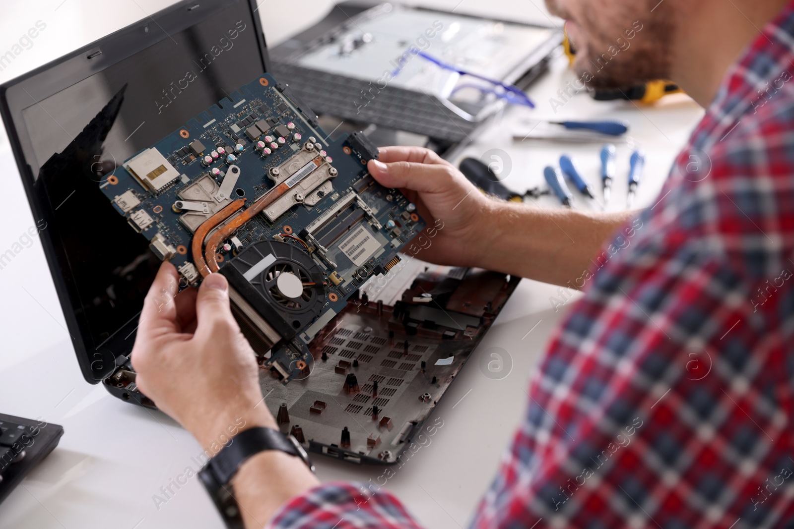 Photo of Man installing motherboard into laptop at white table, closeup