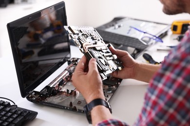 Photo of Man installing motherboard into laptop at white table, closeup