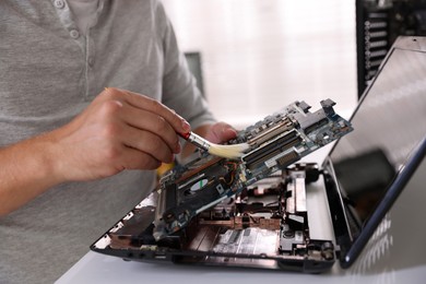 Photo of Man cleaning motherboard with brush at white table, closeup