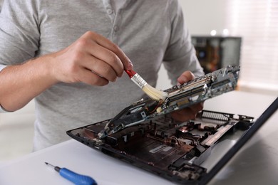 Photo of Man cleaning motherboard with brush at white table, closeup