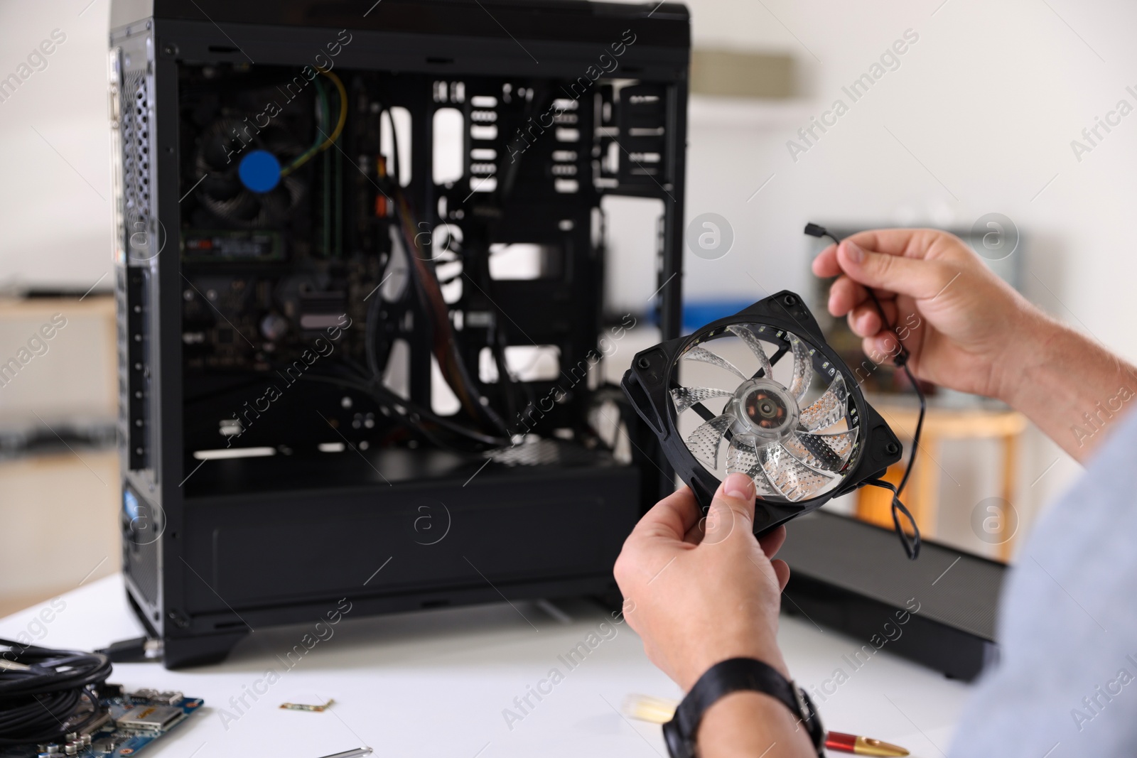 Photo of Man installing fan into computer at white table, closeup