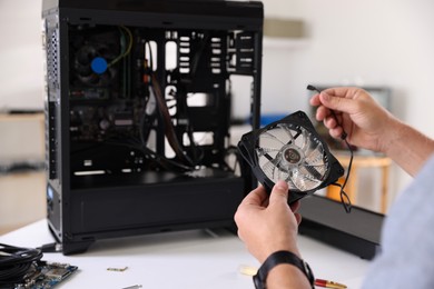 Photo of Man installing fan into computer at white table, closeup