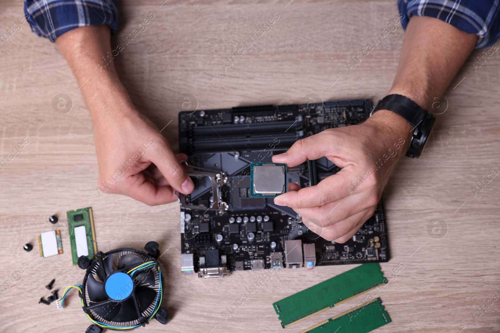 Photo of Man installing computer chip onto motherboard at wooden table, top view