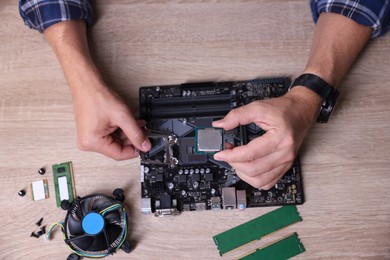 Photo of Man installing computer chip onto motherboard at wooden table, top view