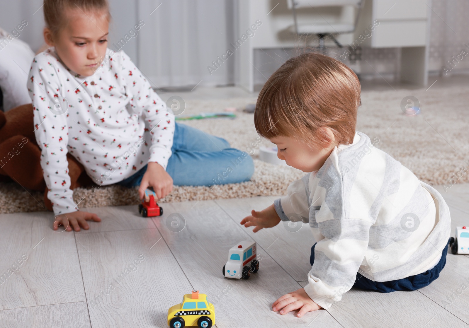 Photo of Sister and brother playing with toy cars on floor indoors